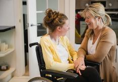 jeune femme handicapée en fauteil sourit à sa maman.