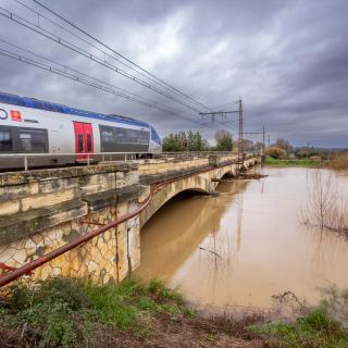 Un train SNCF emprunte un pont au dessus d'une rivière en crue.