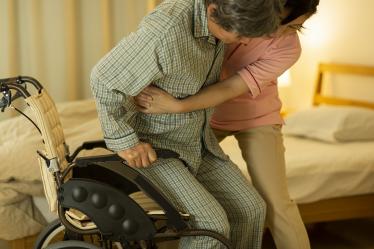 Auxiliaire de vie aidant une personne âgée en fauteuil roulant à se mettre au lit.