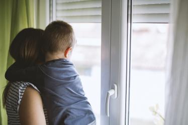 Une mère et son enfant dans les bras regardent par la fenêtre