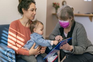 Une jeune femme réfugiée avec son enfant remplit des papiers, aidée d'une dame.