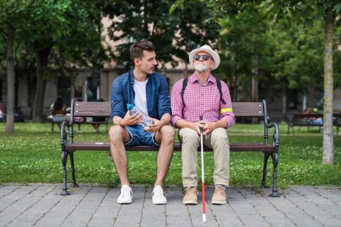 personne âgée non voyante assise sur un banc à côté d'un jeune homme avec qui elle discute