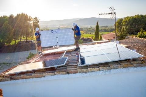 ouvriers installant des panneaux solaires sur le toit d'un bâtiment à la campagne, avec des vignes en arrière plan.
