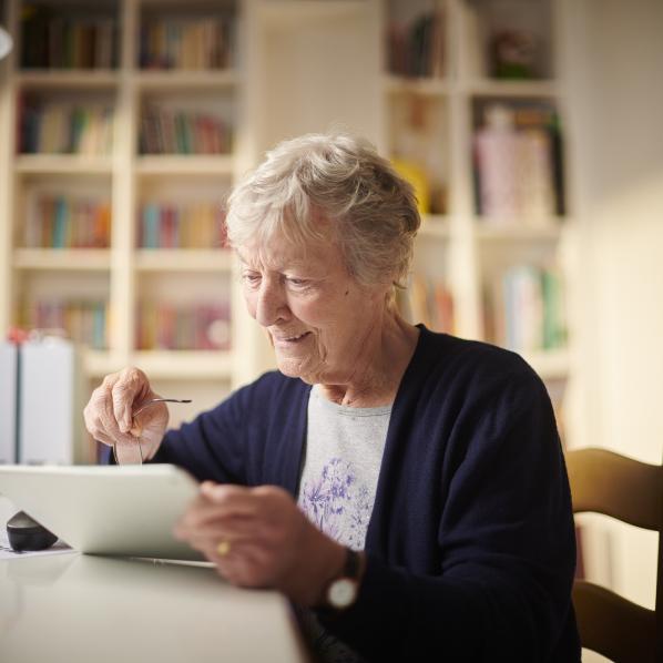 personne âgée assise à une table, en train de naviguer sur une tablette.