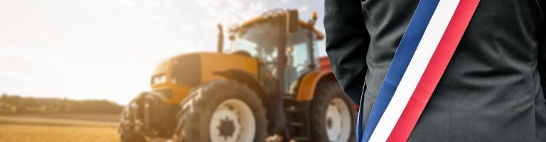 Maire avec son écharpe face à un champ de blé avec tracteur.