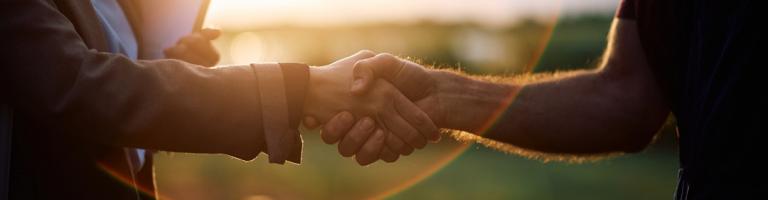 poignée de main entre un maire et un chef de projet territorial, au soleil couchant.