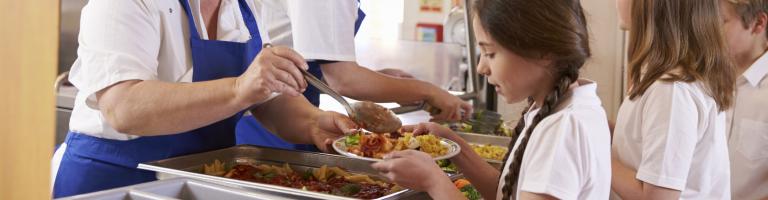 Dame servant le repas à une élève à la cantine