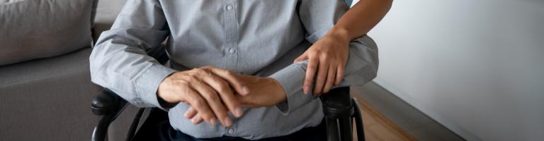 Personne âgée handicapée dans un fauteuil roulant, aidée par une jeune femme.