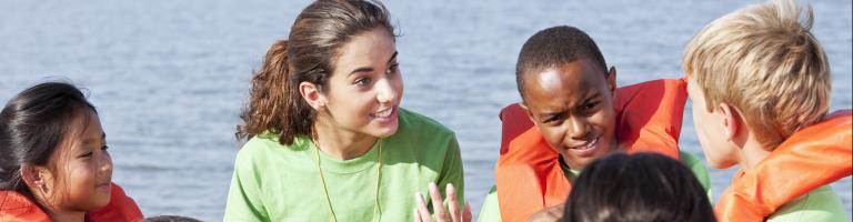 Jeune femme expliquant les consignes de sécurité pour pratiquer le kayak à des enfants.