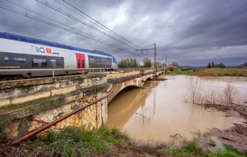 Un train SNCF emprunte un pont au dessus d'une rivière en crue.