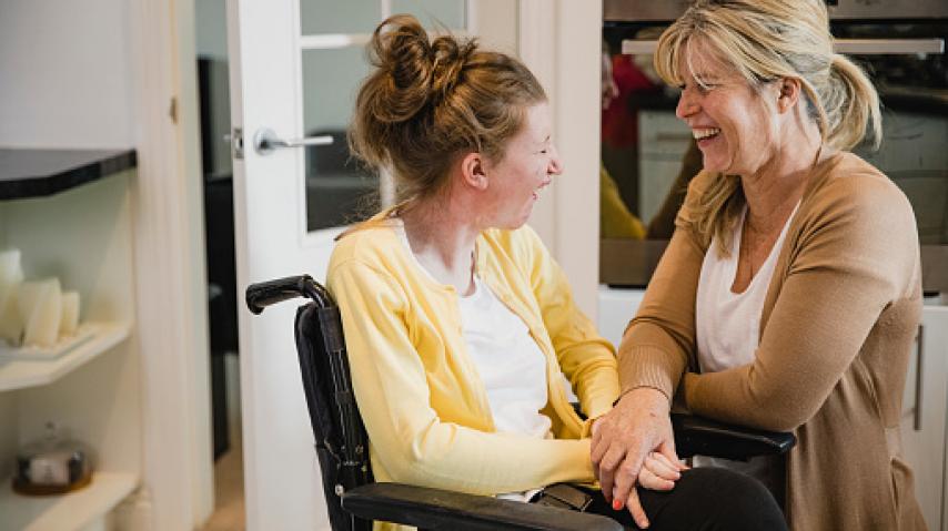 jeune femme handicapée en fauteil sourit à sa maman.