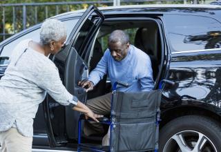 un homme handicapé sort d'une voiture pour s'installer dans son fauteuil roulant avec l'aide d'une femme